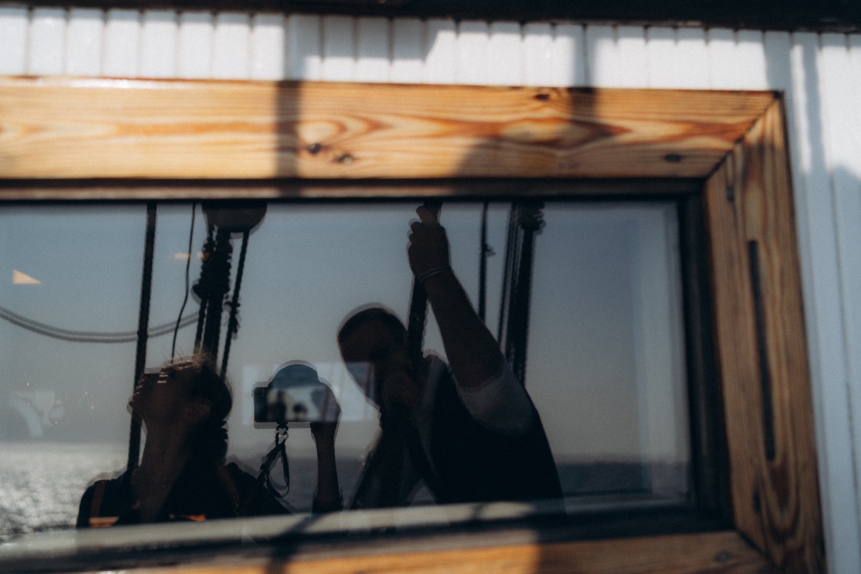 Reflection of a couple filming aboard a sailing ship at sea